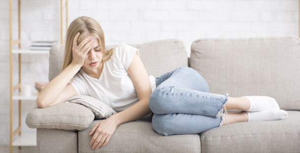 aufgebrachte junge Frau liegt auf Couch und leidet unter Kopfschmerzen - Foto, Bild