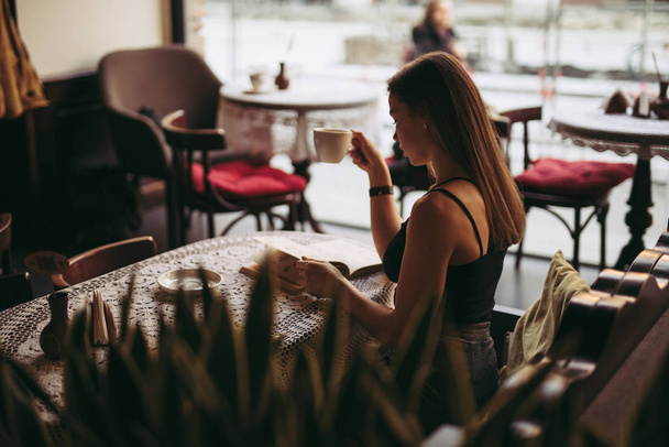 Young woman reading book in cafe and drinking coffee - Foto, imagen