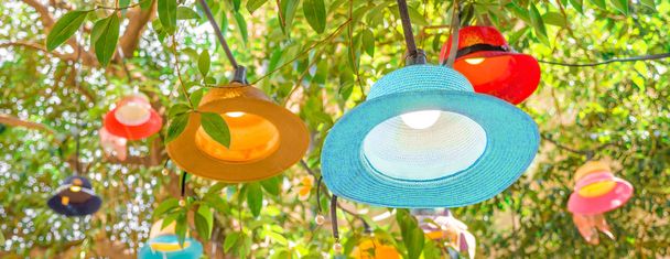 Handmade lampshades background. Cafe outside decor. Original multi-colored lampshades hanging on tree. Green tree decorated with panama lampshades. New life for old hats Closeup - Photo, Image