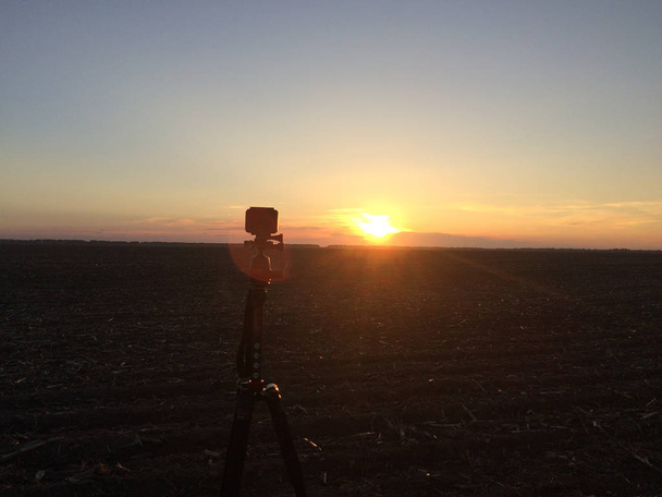 A small camera mounted on a tripod shoots sunset sky. - Photo, Image