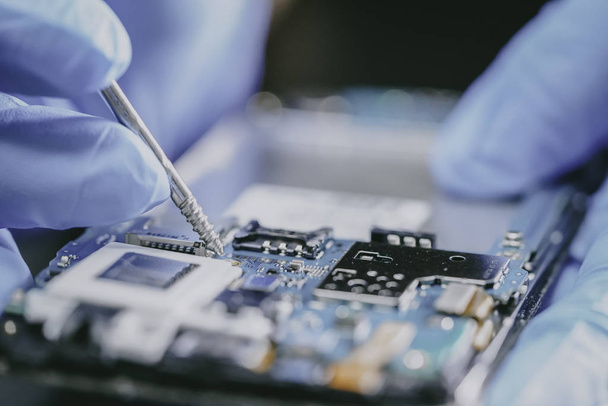E-waste, technicus repareert de binnenkant van de mobiele telefoon door ijzer te solderen. Geïntegreerd circuit. het concept van data, hardware, technicus en technologie. - Foto, afbeelding