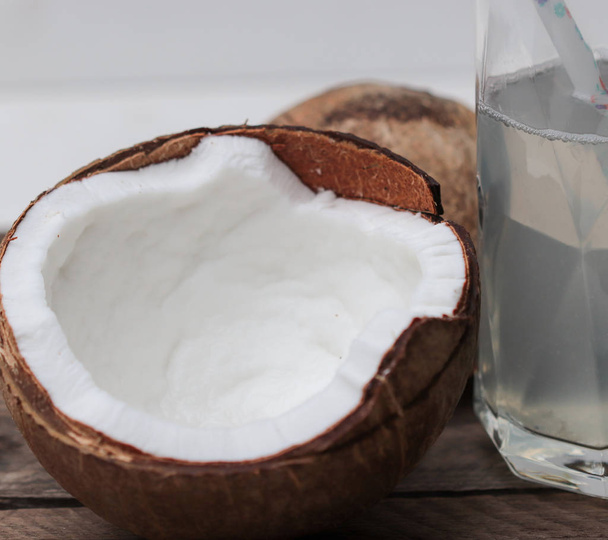 two halves of a coconut on a wooden table and a glass with coconut water - Photo, Image