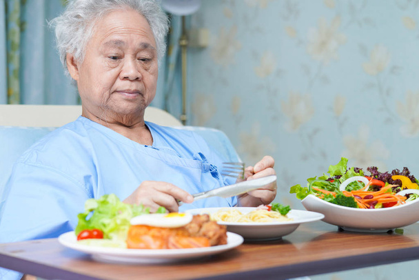 Asian senior or elderly old lady woman patient eating breakfast healthy food with hope and happy while sitting and hungry on bed in hospital - Foto, Imagen