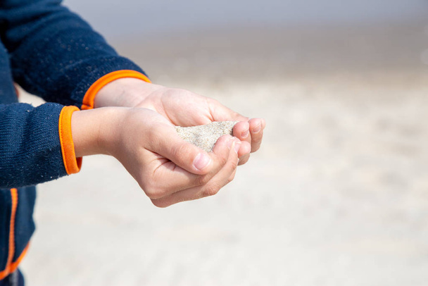un petit garçon laisse lentement couler le sable à travers ses mains dispersées b
 - Photo, image
