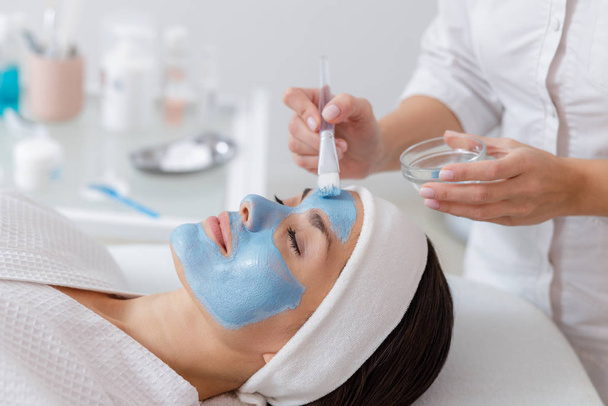 Beautician applying blue mask on woman face - Foto, Bild