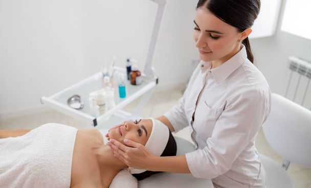 Smiling masseuse massaging face of young woman - Photo, Image