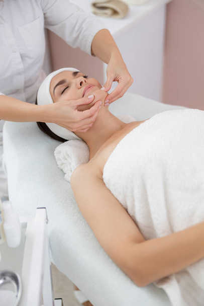 Charming young woman enjoying face massage at spa salon - Foto, afbeelding