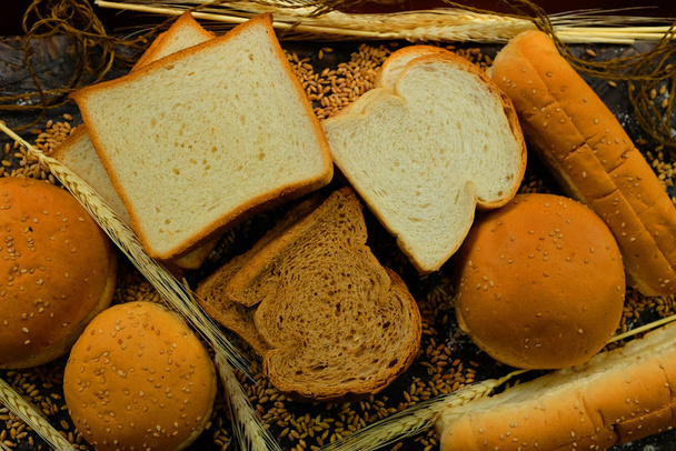 Hamburger breads, hot dogs, fully organic square breads, freshly prepared and baked on black background with wheat ears and wheat in bakery - Photo, Image