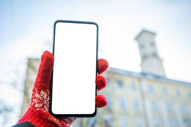 mão mulher em luvas vermelhas segurando telefone com tela branca lviv prefeitura no fundo
 - Foto, Imagem