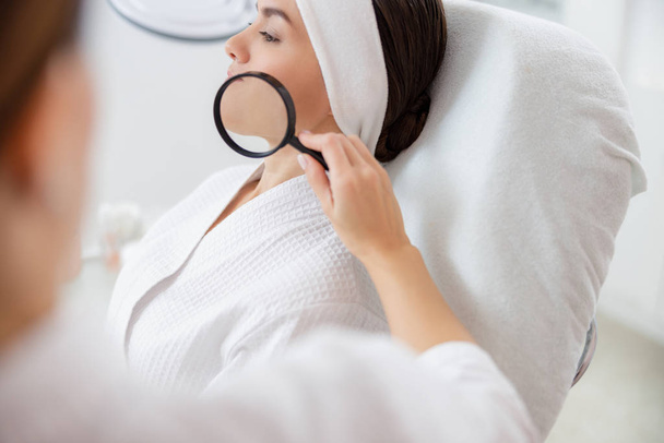 Cosmetologist examining lady skin with magnifying glass - Foto, Bild