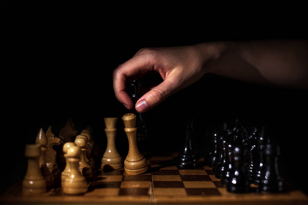 placed chess pieces on a dark background, the concept of confrontation, fair and unfair play, political games, rivalry in business, hand with chess figure has dropped another piece - Foto, afbeelding