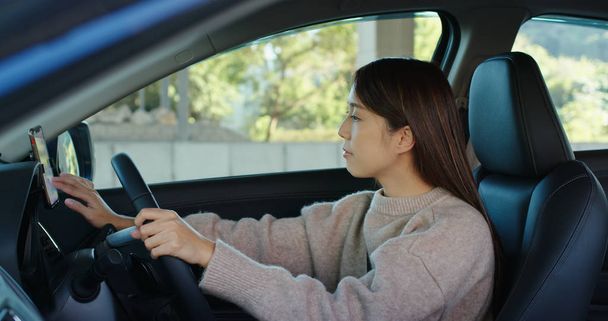 Nainen asettaa GPS sijainnin matkapuhelimeen auton sisällä
 - Valokuva, kuva