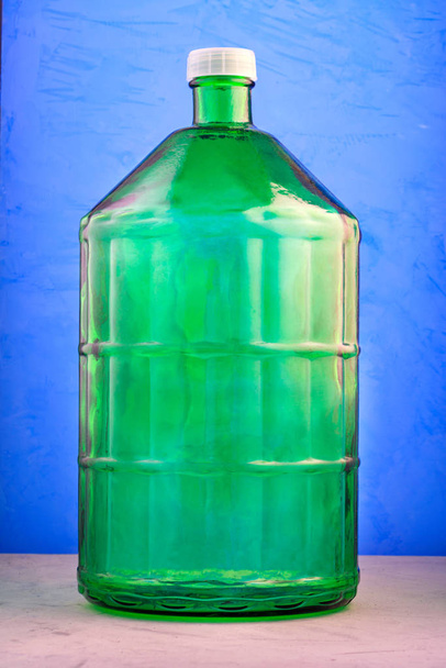 Ένα γυάλινο βάζο 22 λίτρων είναι κατασκευασμένο από παχύ πράσινο γυαλί, εικόνα σε μπλε φόντο. - Φωτογραφία, εικόνα