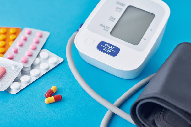 Digitaalinen verenpainemittari ja lääketieteelliset pillerit sinisellä taustalla. Terveydenhuollon ja lääketieteen käsite
 - Valokuva, kuva