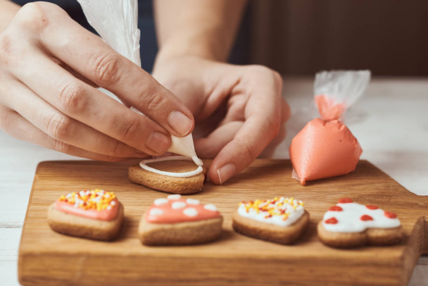 Διακόσμηση μπισκότων μελόψωμο με άχνη. Γυναικείο χέρι διακοσμούν τα μπισκότα σε σχήμα καρδιάς, closeup - Φωτογραφία, εικόνα