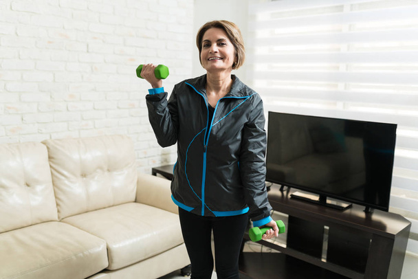 Sonriente mujer caucásica mayor haciendo ejercicio con mancuernas en casa
 - Foto, imagen