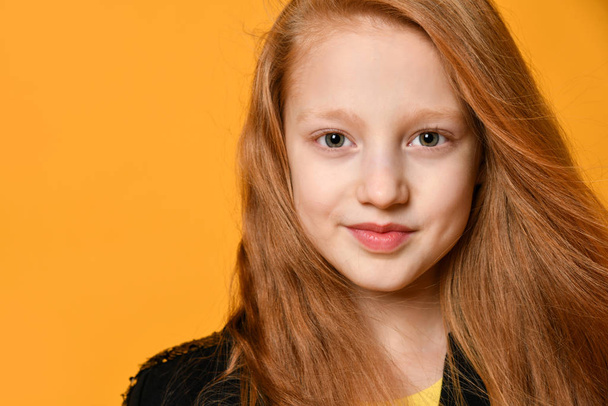 Red-haired teenage kid in black jacket. She is smiling and looking at you, posing against orange studio background. Close up - Foto, Bild