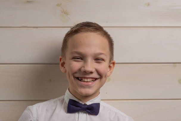 A boy of 10 years old is smiling on the background of a wooden w - Foto, afbeelding