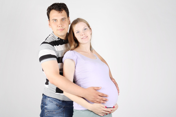 Handsome man embraces belly of happy pregnant woman on grey back - Zdjęcie, obraz