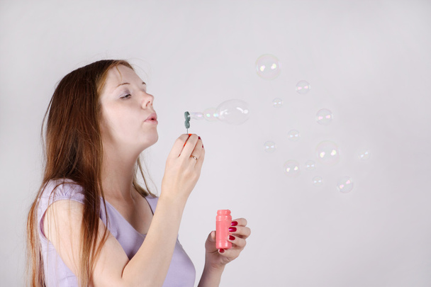 Beautiful woman with long hair blows soap bubbles on grey backgr - Photo, Image
