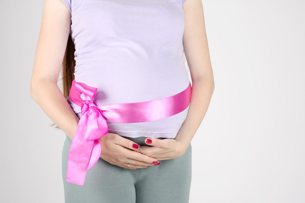 Stomach of pregnant woman with pink ribbon on grey background. - Foto, immagini