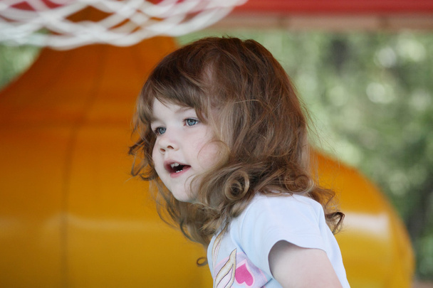 Little pretty happy girl in yellow inflatable trampoline looks a - Fotografie, Obrázek