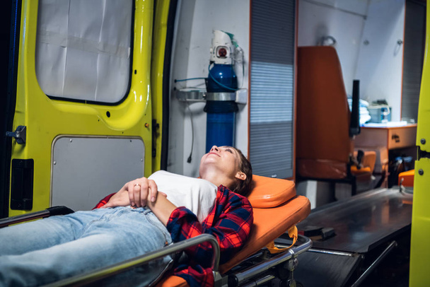 Женщина лежит на носилках в машине скорой помощи
 - Фото, изображение