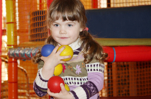 Little cute girl with multicolored balls in hands on playground. - Valokuva, kuva