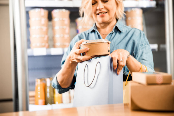 Happy mature lady standing near cashier desk - Foto, afbeelding