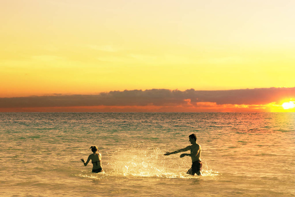 Ranta hauska pari leikkii merivedessä roiskeita vettä toisiaan auringonlaskun aikaan. Kesäloma
. - Valokuva, kuva