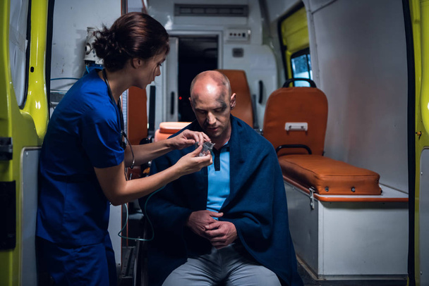 Ambulance auto, verpleegster zet zuurstof masker op man in deken - Foto, afbeelding