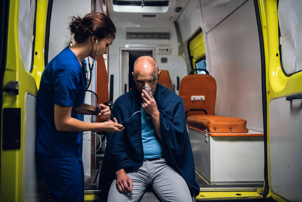 Infirmière en uniforme avec stéthoscope et homme assis dans un masque à oxygène dans une couverture
 - Photo, image