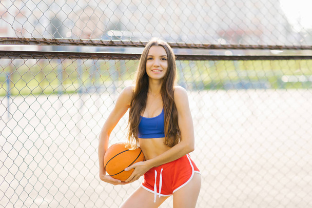 dziewczyna w krótkich czerwonych spodenkach i niebieski top posiada piłkę do koszykówki  - Zdjęcie, obraz