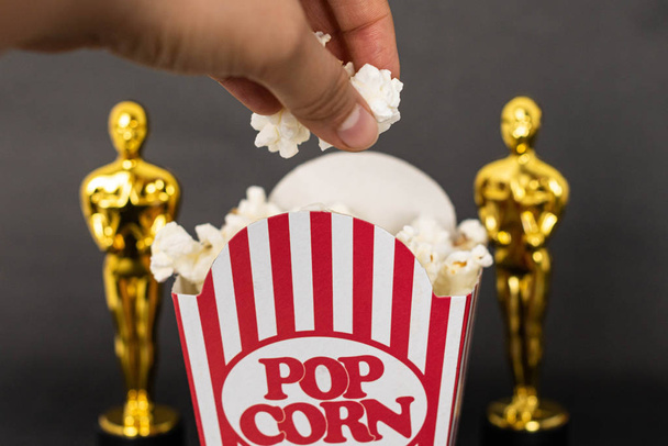 xalapa, veracruz, mexiko - 31. Januar 2020: Frau greift nach frischem Popcorn einer klassischen Popcornbox und zwei verschwommenen Plastik-Oscar-Auszeichnungen auf schwarzem Hintergrund - Foto, Bild