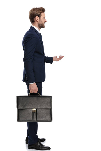 joven hombre de negocios en traje azul marino sosteniendo la maleta y de pie
 - Foto, imagen