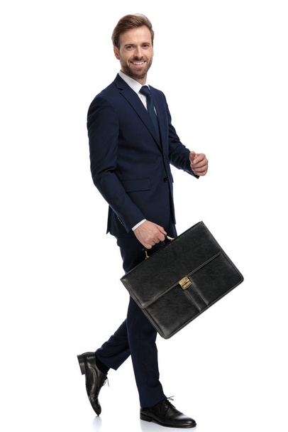 χαρούμενος νεαρός επιχειρηματίας κρατώντας βαλίτσα και χαμογελώντας - Φωτογραφία, εικόνα