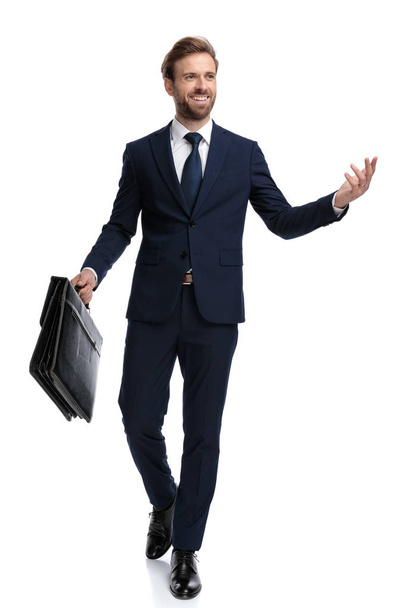 happy young businessman holding suitcase and presenting to side - Foto, imagen