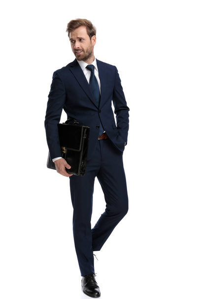 sexy young man in navy blue suit holding suitcase in fashion pos - Fotografie, Obrázek
