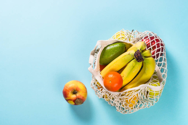 Mesh bag with fruits on color background. - Foto, Imagen