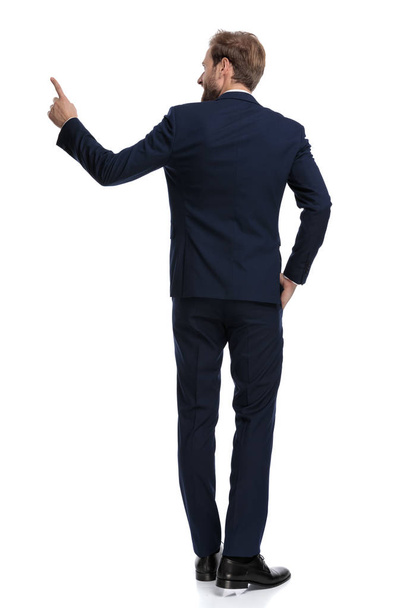 smiling bussinesman in navy blue suit pointing finger to side - Фото, изображение