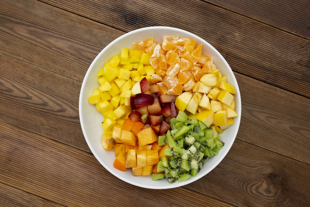 Fresh fruits salad - mango, citrus, kiwi fruit, plum and persimmon. Wooden background, flat lay, top view healthy food. Smoothie mix. - Photo, image