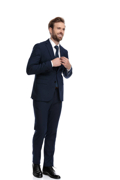 happy businessman in navy blue suit arranging tie - Фото, изображение