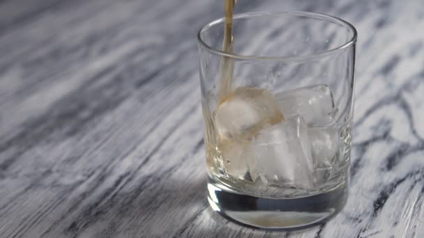 Złota whisky jest wlewana do szklanego kubka z kostkami lodu na starym drewnianym szarym blacie. Zwolniony ruch - Materiał filmowy, wideo