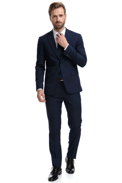 confiado hombre de negocios en traje azul marino ajustando corbata
 - Foto, Imagen