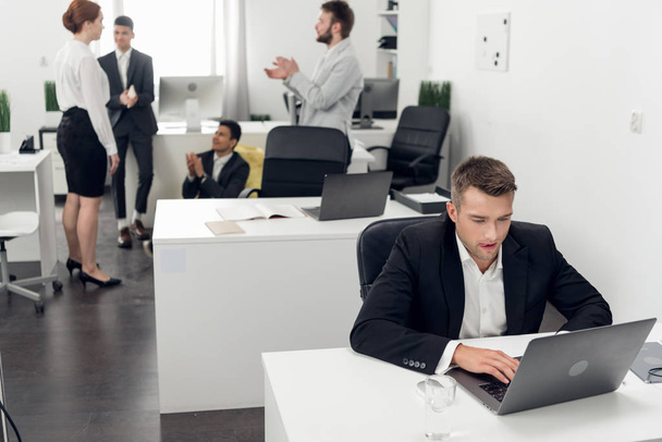 Мужчины и женщины имеют перерыв во время рабочего дня в офисе, сосредоточиться на молодом человеке, работающем на ноутбуке
 - Фото, изображение