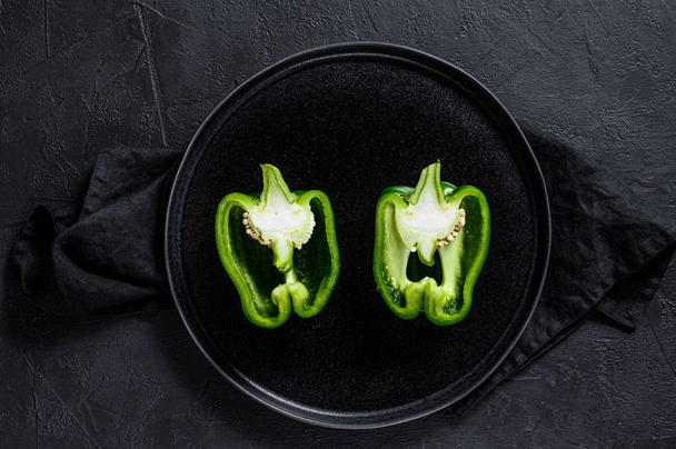 Cut green sweet pepper, two halves. Black background. Top view. - Photo, image