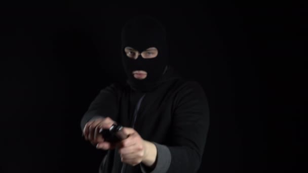 Un uomo con una maschera di passamontagna sta con una pistola. Il delinquente punta la pistola e spara alla telecamera. Su uno sfondo nero. - Filmati, video