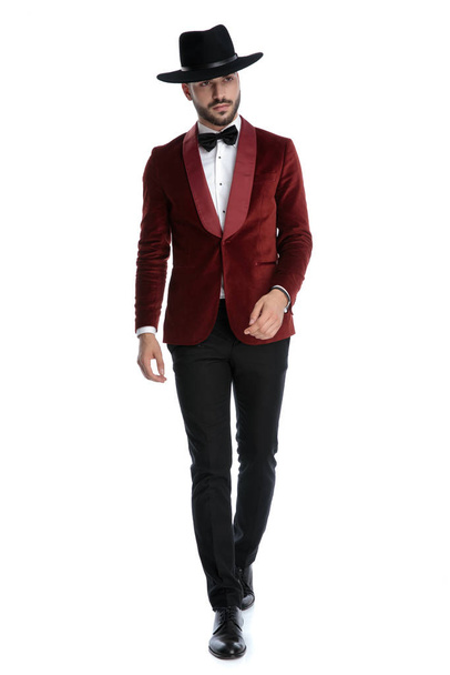 confident young man in red velvet tuxedo wearing hat and walking - Foto, Imagen