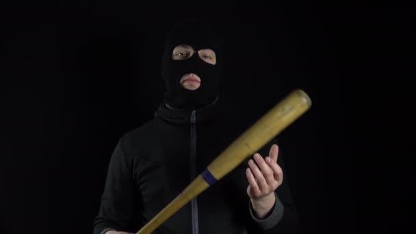 A man in a balaclava mask is standing with a baseball bat. A gangster is holding a baseball bat on a black background. - Footage, Video