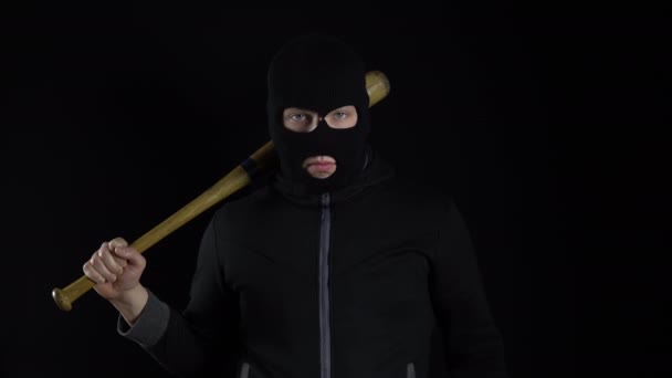 A man in a balaclava mask is standing with a baseball bat. A bandit stands on a black background with a baseball bat over his shoulder. - Footage, Video